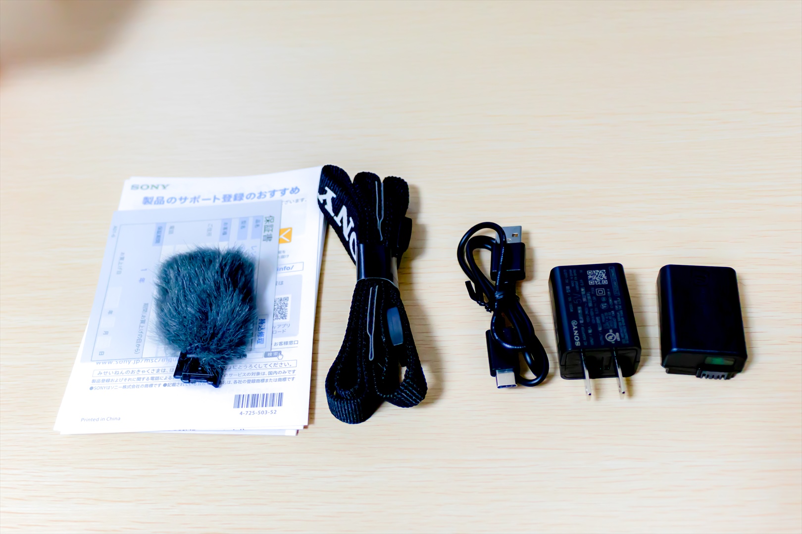 ZV-E10の付属品です。左から説明書、保証書、風防（通称もふもふ）、ストラップ、USBケーブル（TypeA-TypeC）、USB接続の充電アダプター、バッテリーです。